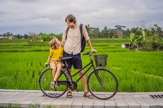 Pai e filho andam de bicicleta em um campo de arroz em ubud bali viajam para bali com o conceito de crianças