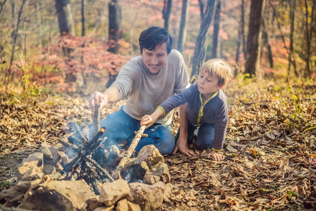 Pai e filho animado sentado na barraca na floresta acampando com fogueira