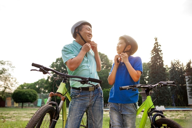 Pai e filho asiáticos colocam capacete na cabeça antes de andar de bicicleta sênior coreano com filho ao ar livre