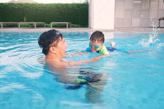 Pai e filho asiáticos fazendo aula de natação na piscina