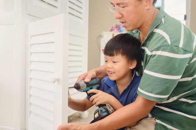 Pai e filho asiáticos trabalhando com chave de fenda elétrica sem fio Pai e filho montando móveis