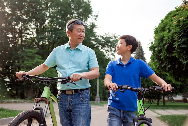 pai e filho asiáticos velhos andam de bicicleta juntos no parque sênior coreano e avô estão ativos