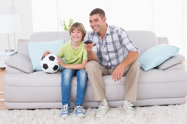 Pai e filho assistindo partida de futebol no sofá