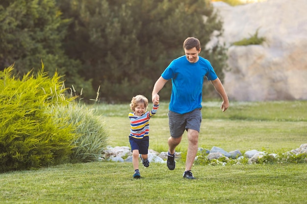 Pai e filho ativos jogam juntos e correm no parque verde de férias