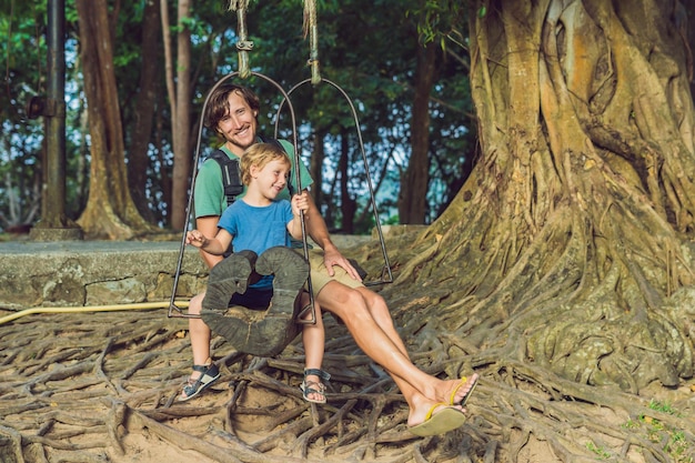 Pai e filho balançando em um velho balanço contra o fundo das raízes da árvore