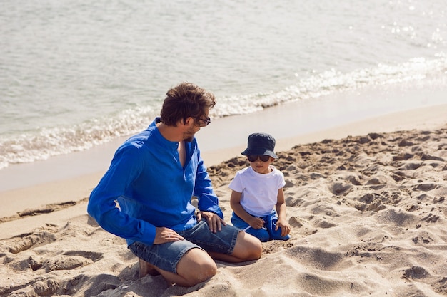 Pai e filho brincam de óculos escuros na praia no verão com roupas azuis durante as férias