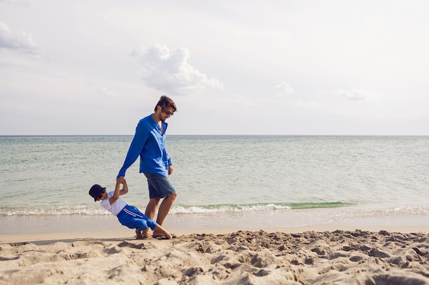 Pai e filho brincam na praia no verão com roupas azuis durante as férias