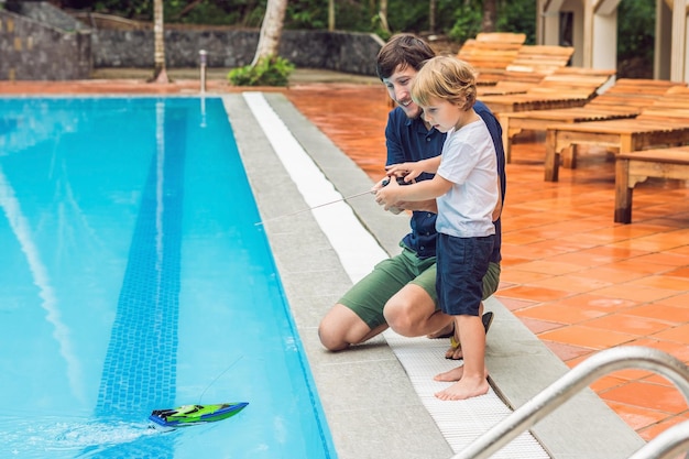 Pai e filho brincando com um barco de controle remoto na piscina.