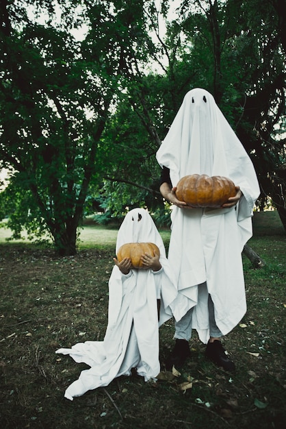 Pai e filho brincando de fantasmas com lençóis brancos no jardim