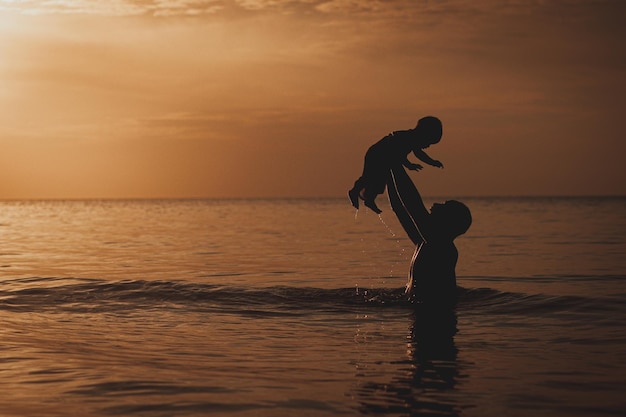 Pai e filho brincando na praia na hora do pôr do sol. Pessoas se divertindo em campo.