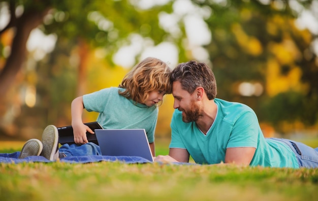 Pai e filho brincando ou estudando com o laptop no parque criança com o papai aprendendo lição blogging