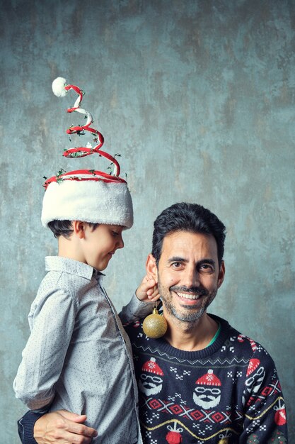 Pai e filho com chapéu de natal engraçado colocando uma bola dourada de natal como um brinco