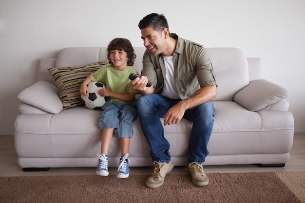 Pai e filho com futebol assistindo tv na sala de estar