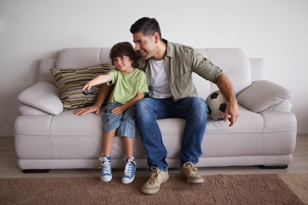 Pai e filho com futebol assistindo tv na sala de estar