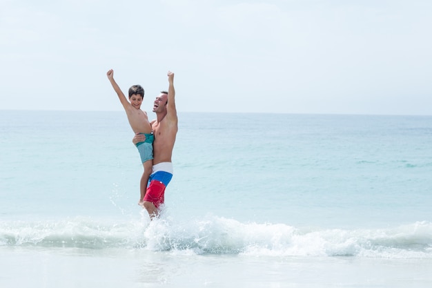 Pai e filho com os braços levantados desfrutando na praia