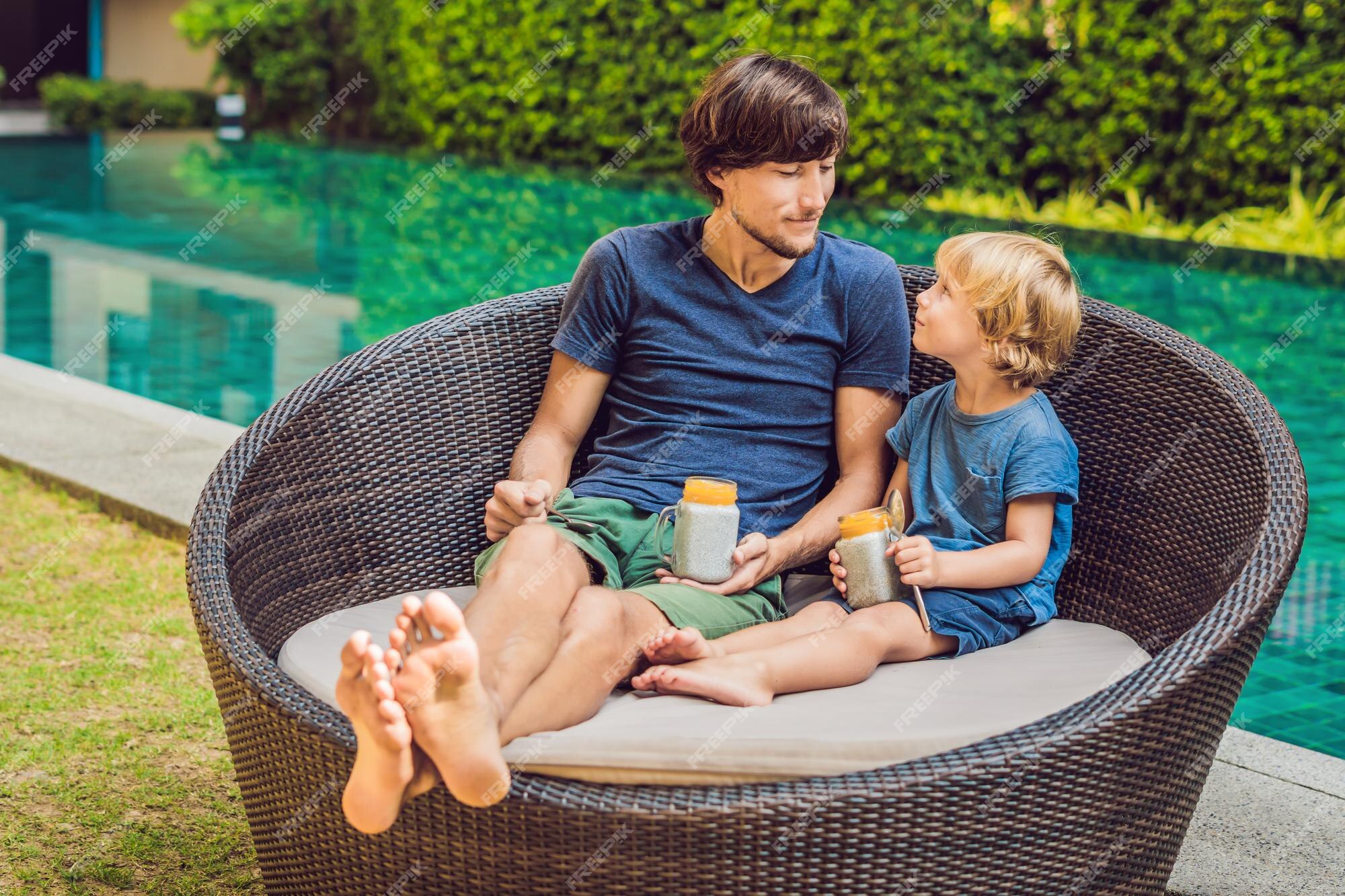 Pai e filho comem sobremesa com sementes de chia e manga à beira da piscina  pela manhã. alimentação saudável, comida vegetariana, dieta e conceito de  pessoas