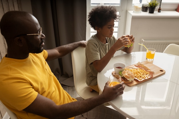 Foto pai e filho comendo batatas fritas e hambúrgueres juntos