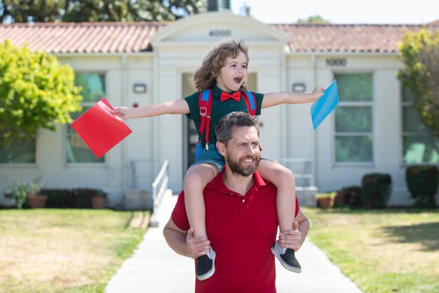 Pai e filho correm com o pai depois de voltar da escola. Escola, família, educação e conceito ao ar livre, primeiro dia de outono. Pai e filho se divertindo perto do pátio da escola. Conceito de família amigável.