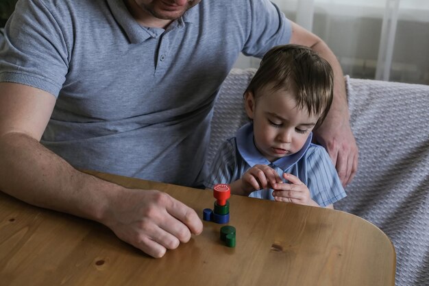 Pai e filho de 1 ano brincam com estatuetas de madeira em casa Desenvolvimento de habilidades motoras finas