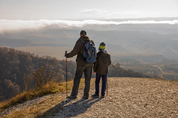 Pai e filho de pé no topo de uma montanha e olhando para longe