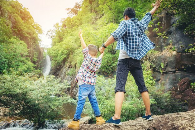 Pai e filho em pé viajam juntos e braços abertos comemoram suas férias com grande floresta