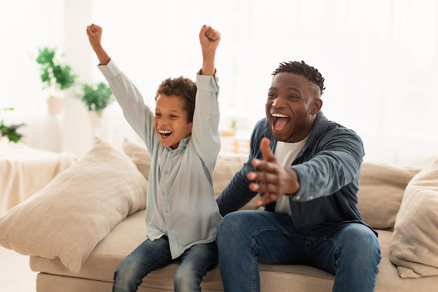 Pai e filho emocionais a ver desporto na televisão em casa.