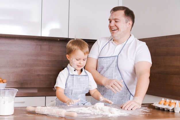 Pai e filho estão de pé na sala de cozinha e fazendo massa juntos Eles