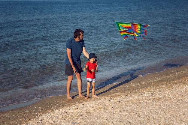 Pai e filho estão em uma praia de areia à beira-mar e lançam uma pipa de brinquedo listrada no verão nas férias