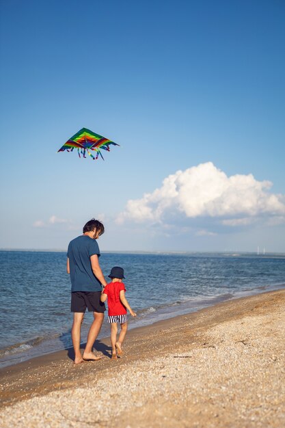 Pai e filho estão em uma praia de areia à beira-mar e lançam uma pipa de brinquedo listrada no verão nas férias