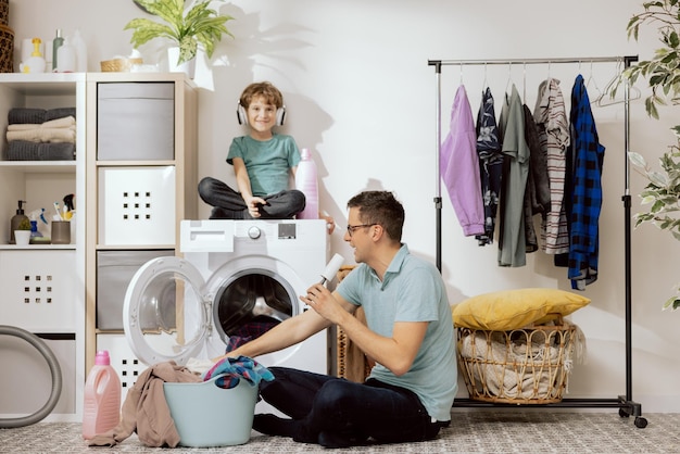 Pai e filho estão lavando roupas, uma criança pequena se senta na máquina de lavar ajudando o pai lis