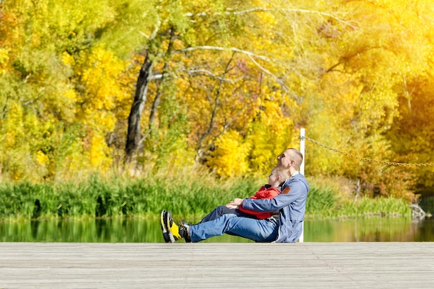 Pai e filho estão sentados na doca Vista lateral ensolarada de outono