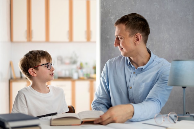 Pai e filho estudam matérias escolares em casa. Jovem professor ensina um aluno. Educação escolar em casa.