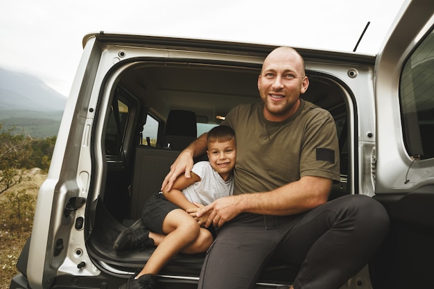 Pai e filho felizes sentados no porta-malas do carro