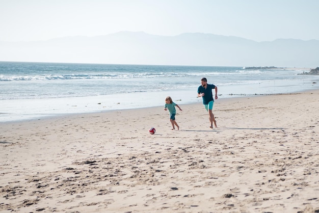 Pai e filho jogam futebol ou futebol na praia, pai e filho em um dia de verão