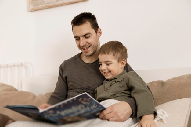 Pai e filho lendo um livro na cama em casa. Jovem atraente e menino descansando no quarto. Cores naturais da terra. Ambiente aconchegante. O pai lê um conto de fadas para o filho.