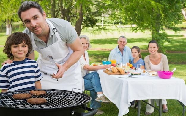 Foto pai e filho na churrasqueira com a família almoçando no parque