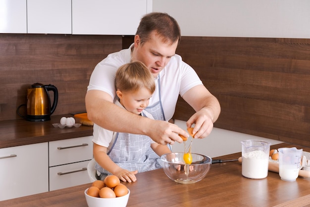 Pai e filho na cozinha pai ensina criança a quebrar ovos em uma tigela Cozinhar