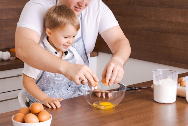 Pai e filho na cozinha pai ensina criança a quebrar ovos em uma tigela Cozinhar