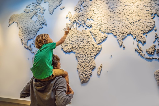 Pai e filho no fundo de um mapa do mundo com um avião nas mãos Conceito de viagem
