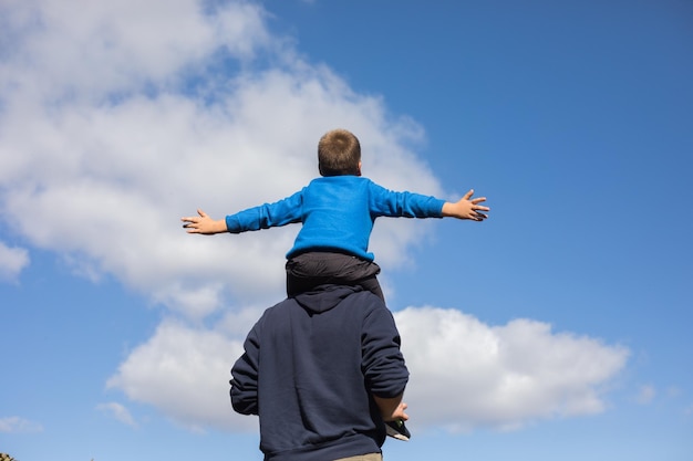 Pai e filho no parque pai carrega seu filho no pescoço através do brilho do sol no céu