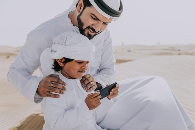 Pai e filho olhando para o smartphone enquanto estão sentados no deserto