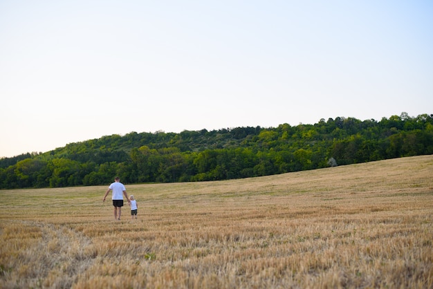 Pai e filho pequeno estão andando por um campo de trigo segado.