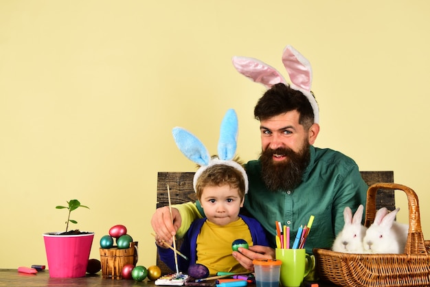 Foto pai e filho pintando ovos de páscoa, criança fofa com orelhas de coelho no dia de páscoa