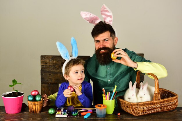 Pai e filho pintando ovos de páscoa, criança fofa com orelhas de coelho no dia de páscoa