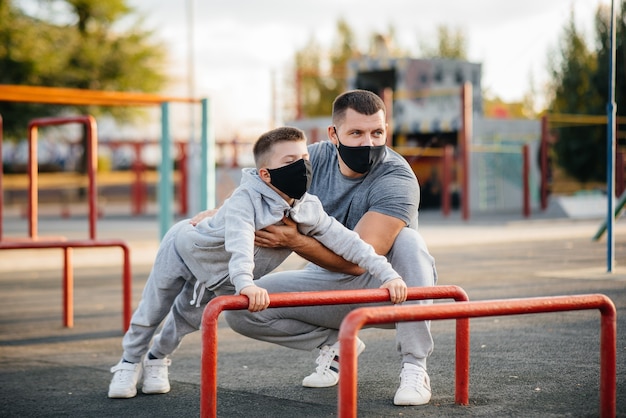 Pai e filho praticam esportes no campo de esportes com máscaras durante o pôr do sol. Paternidade saudável e estilo de vida saudável.