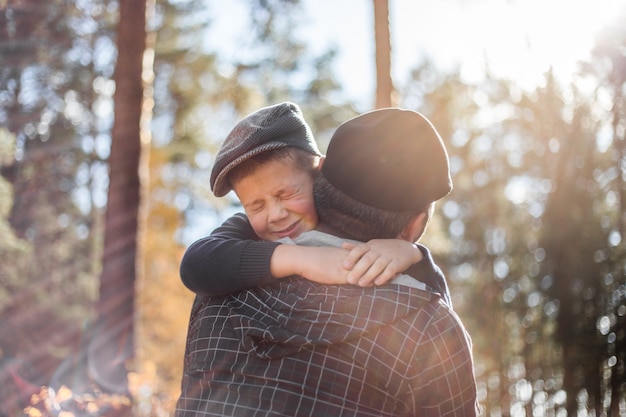 Pai e filho se abraçando e se abraçando na floresta. Feliz pai e filho menino aproveitando o tempo de outono de férias em um parque ensolarado. As crianças adoram o carinho e a ternura dos pais, uma família adorável.