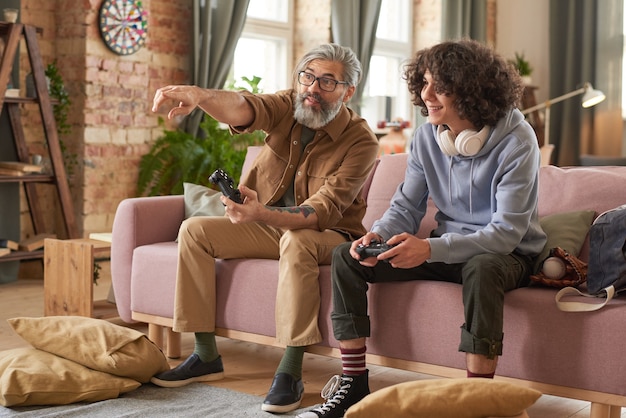 Pai e filho sentados no sofá discutindo o jogo deles enquanto brincam na sala de estar de casa