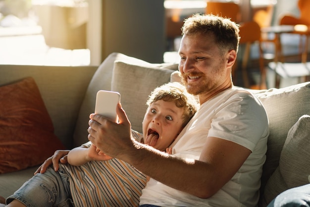 Pai e filho sentam-se relaxando no sofá no corredor do hotel divertindo-se usando o telemóvel
