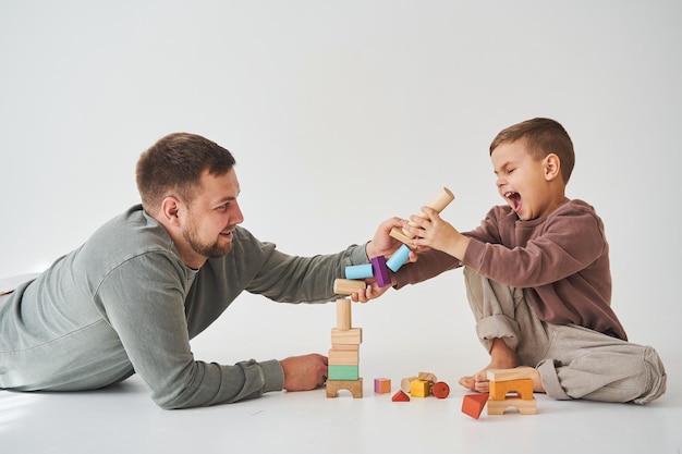 Pai e filho sorrindo se divertindo e brincando de brinquedo de tijolos coloridos em fundo branco Paternidade Pai carinhoso com seu filho