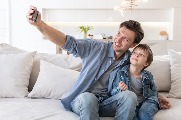 Pai e filho tiram uma selfie enquanto estão sentados no sofá em casa